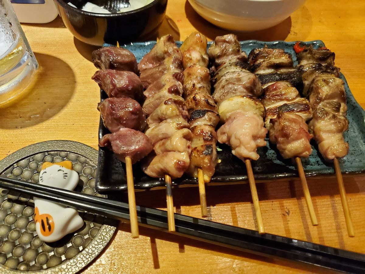 皿いっぱいに並んだ焼き鳥の串と、猫の箸置き